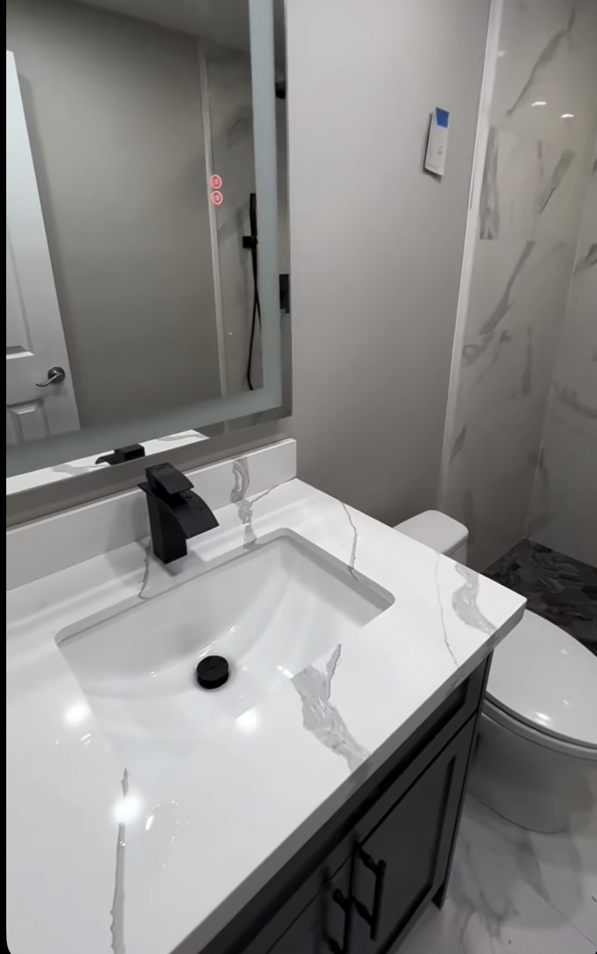 Finished bathroom with marble-look vanity, matte black faucet, backlit mirror, and walk-in shower